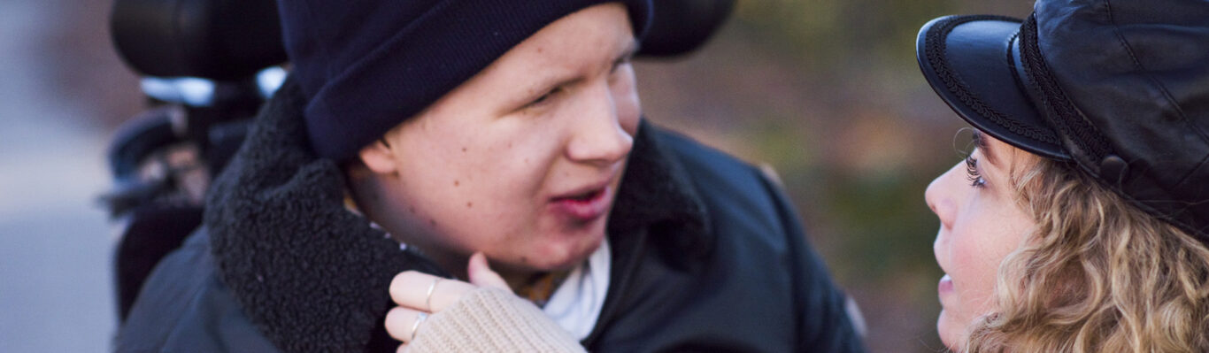 Personlig assistent rättar till halsduken på assistansanvändaren.