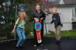 Barn hoppar på en studsmatta. Ett av barnen har stöd av en personlig assistent.