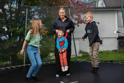 Barn hoppar på en studsmatta. Ett av barnen har stöd av en personlig assistent.