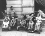 Svart-vitt fotografi med sex personer, varav fem sitter i rullstol.