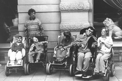 Svart-vitt fotografi med sex personer, varav fem sitter i rullstol.