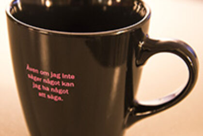Svart kaffemugg med rosa text: "Även om jag inte säger något kan jag ha något att säga"