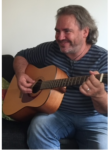 Bild på en leende man med skägg och gitarr.