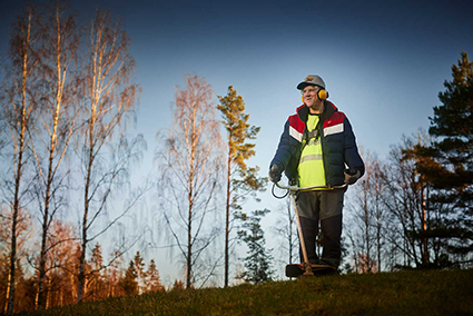 Man med hörselskydd står i en skog under blå himmel.