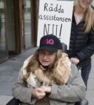 Rullstolsburen kvinna med keps med JAGs logga med demonstrationsskylt Rädda assistansen NU!