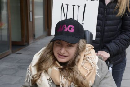 Rullstolsburen kvinna med keps med JAGs logga med demonstrationsskylt Rädda assistansen NU!