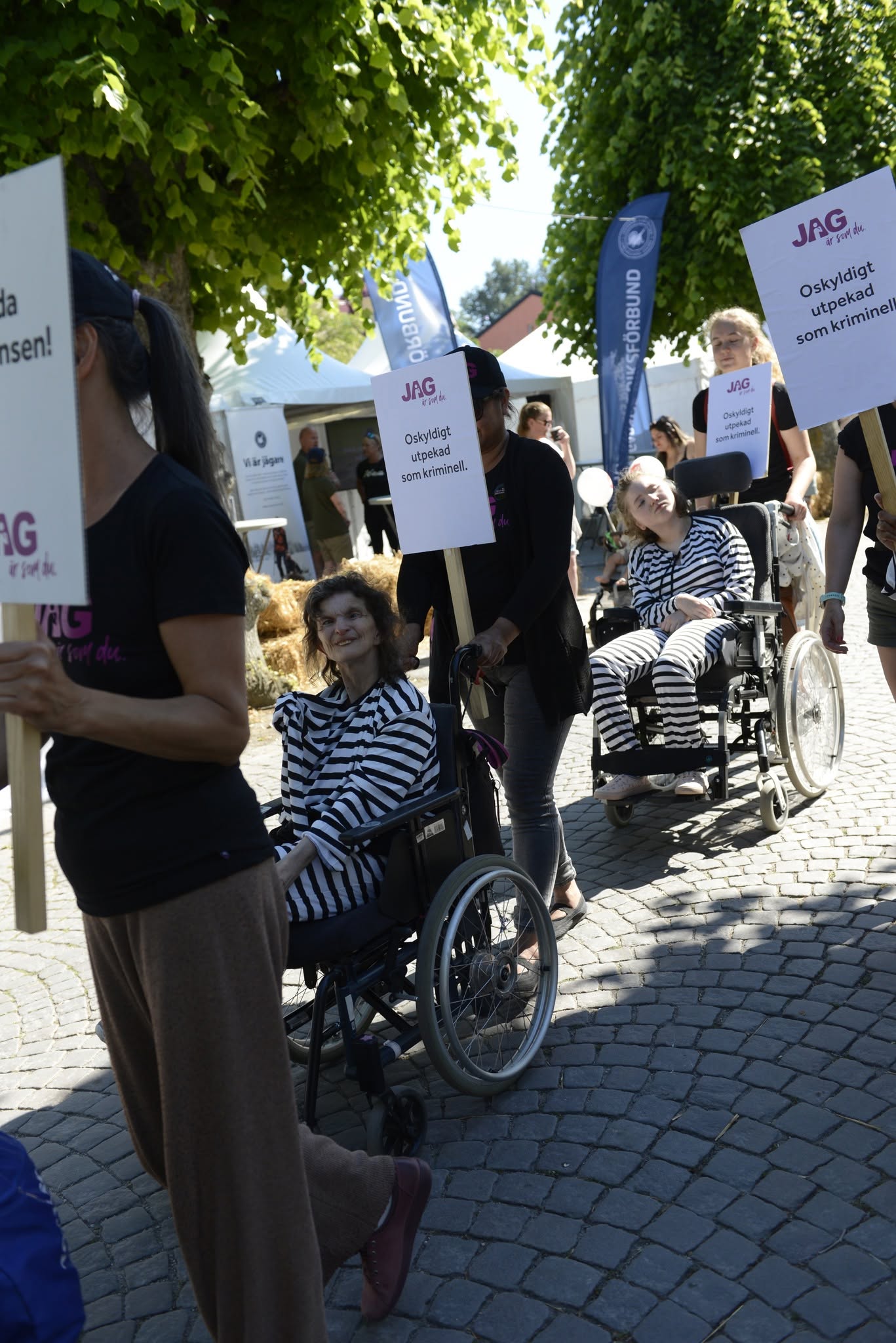 Ett demonstrationståg med rullstolsburna personer i randiga fångdräkter.