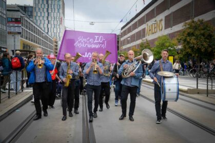 Orkester som leder en karneval framför en rosa banderoll