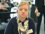 Ung kvinna med blont uppsatt hår som tittar allvarligt in i kameran